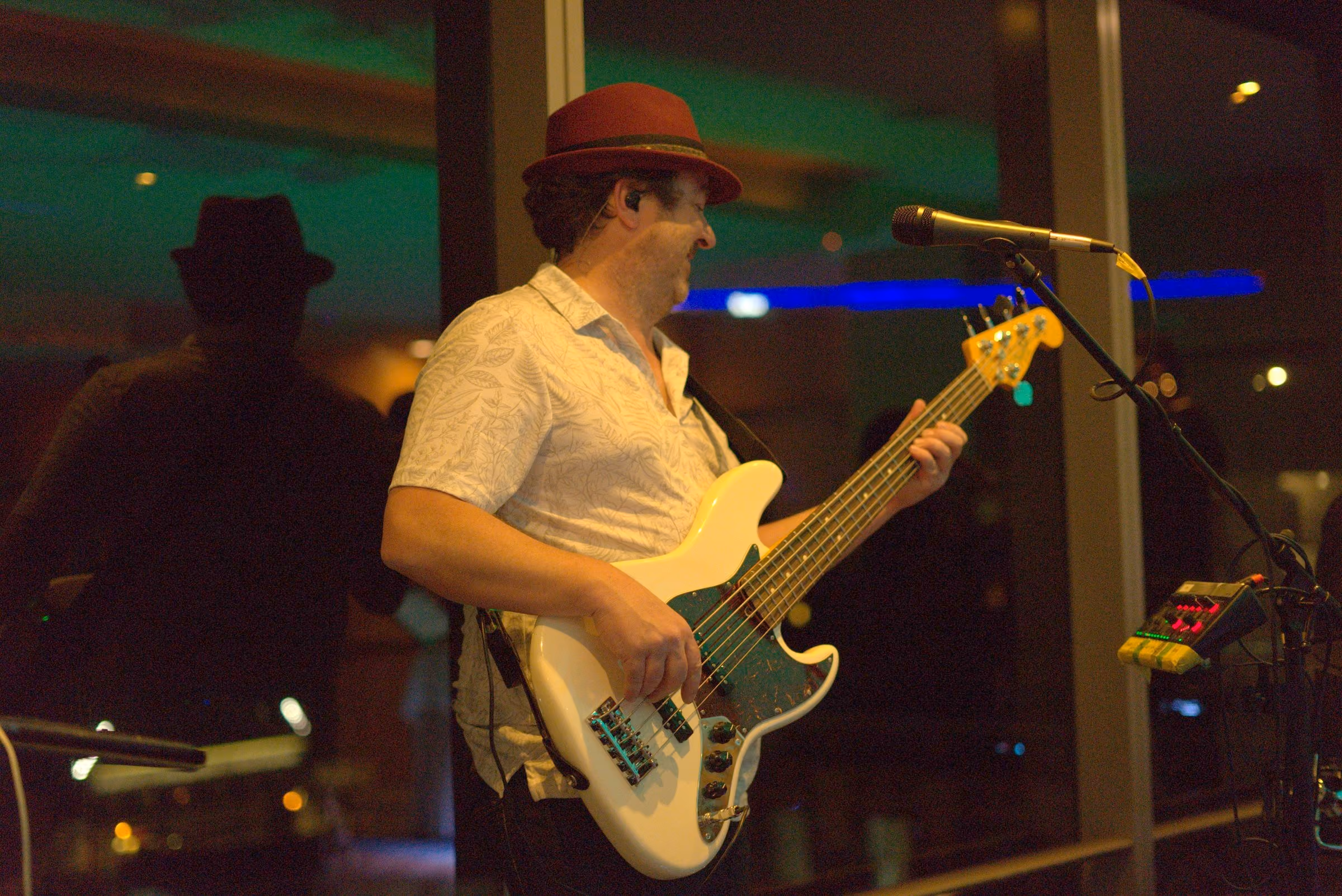 Bass player in a hat and patterned shirt under warm light