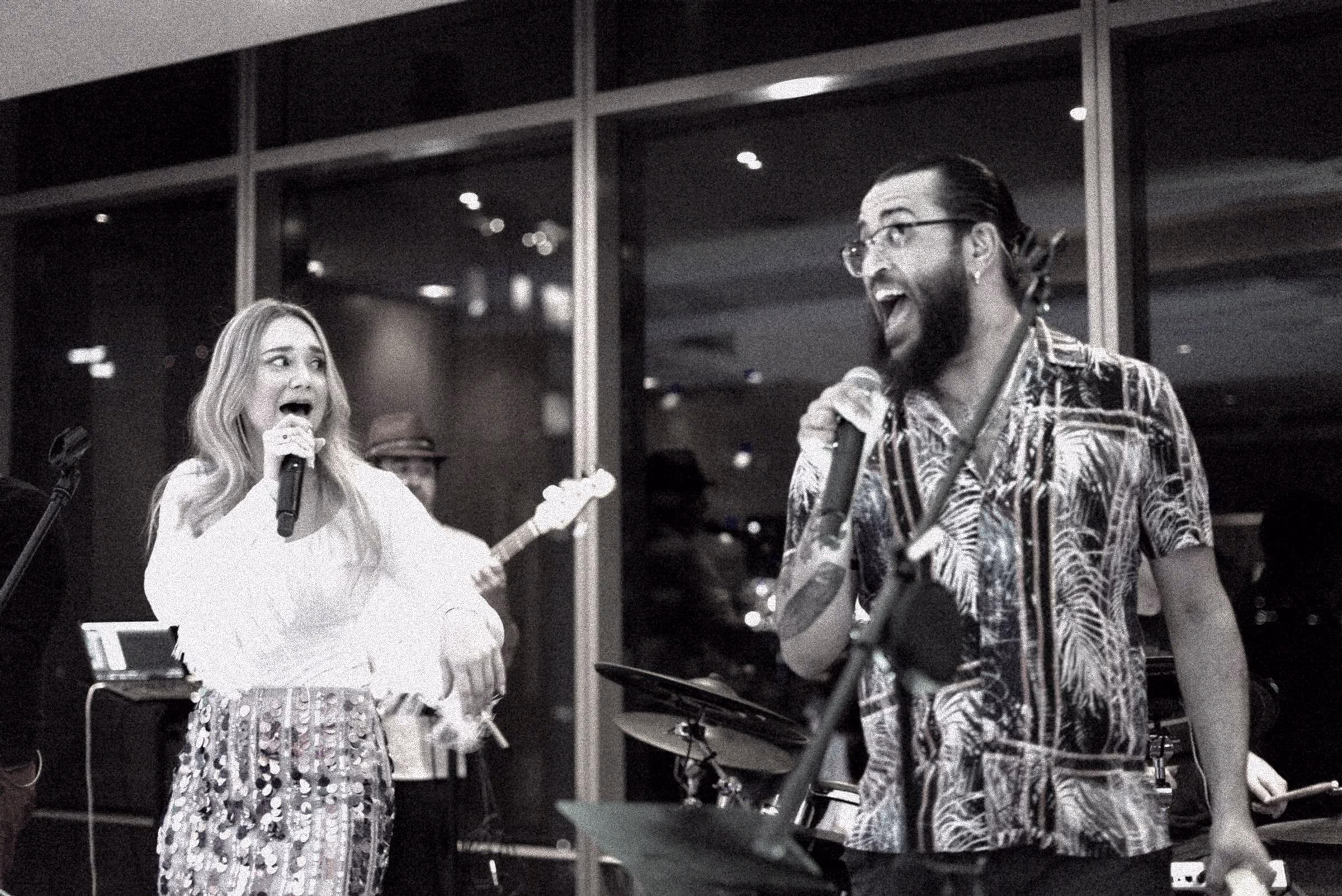 Two singers laughing at their microphones, in black and white