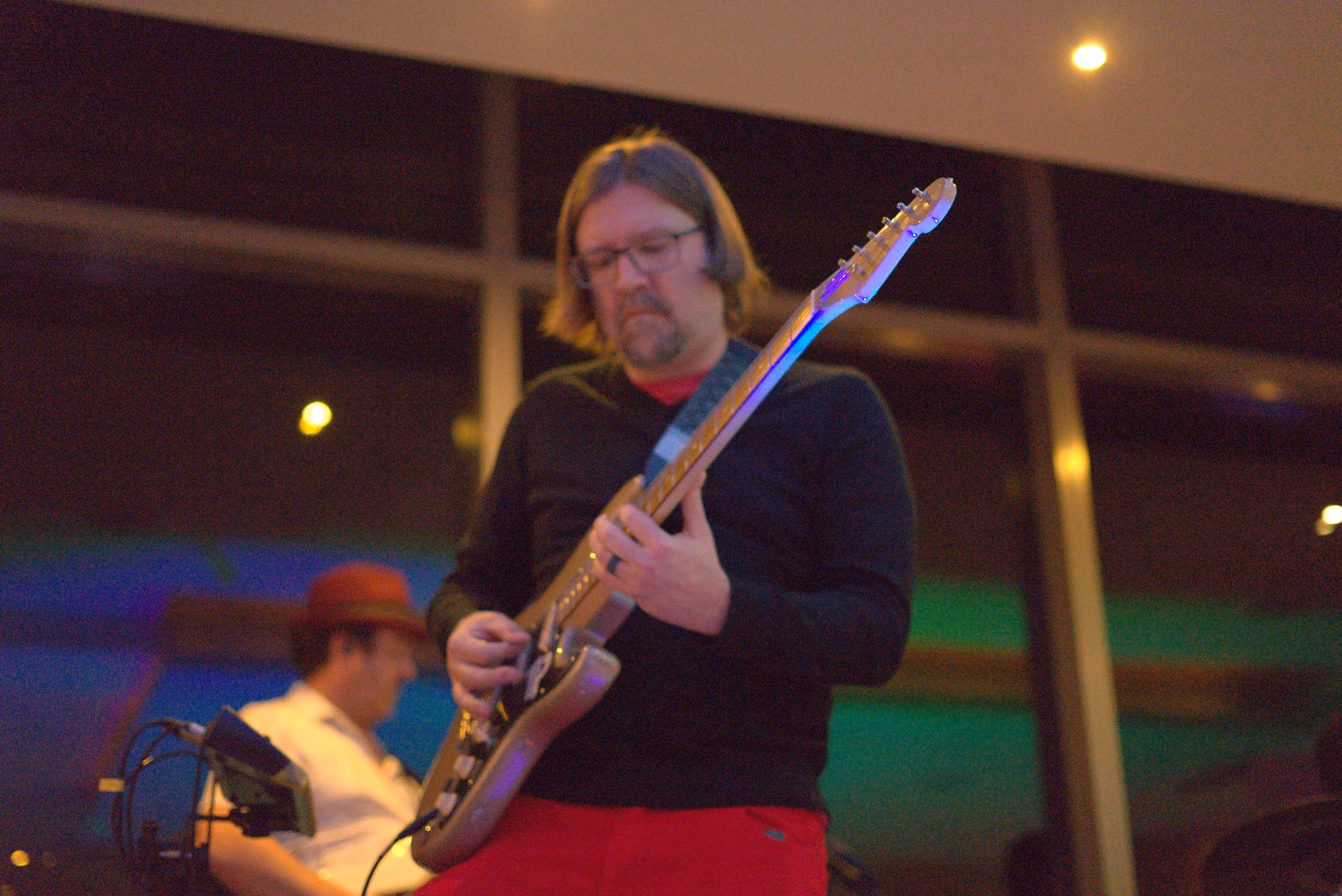 Guitarist in a dark shirt and red trousers playing a white guitar