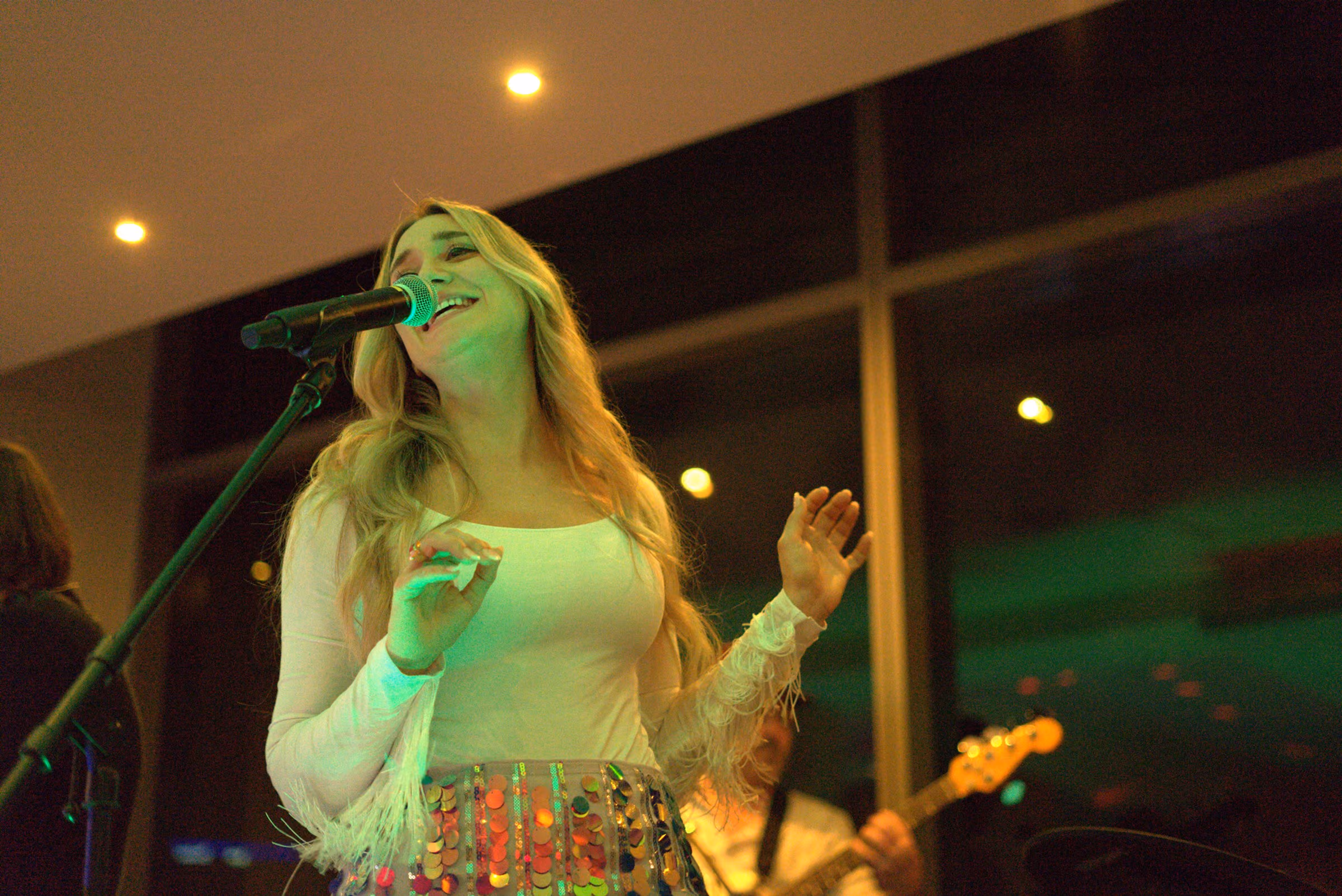 Singer in a white fringed top mid-song, one hand raised, tall windows behind