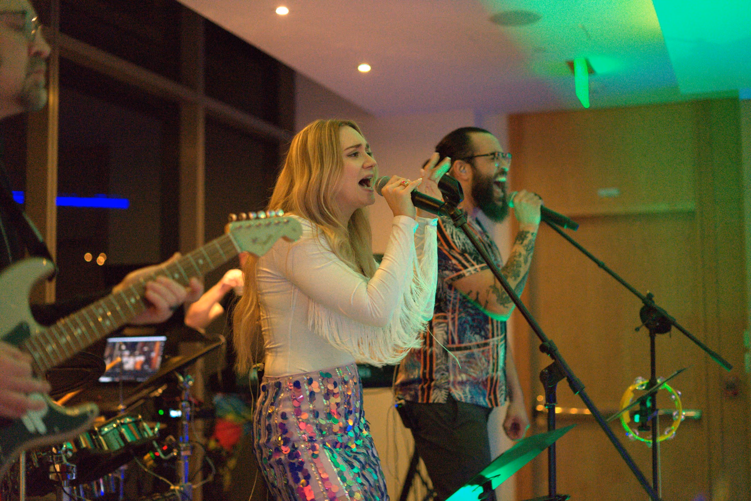 Two singers sharing the front of the stage with a guitarist behind them